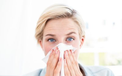 Sick blonde woman blowing her nose in the living room